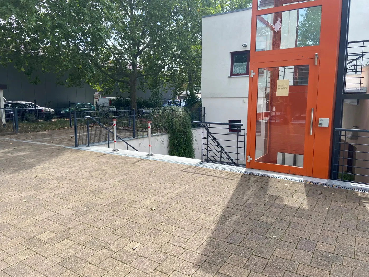 Blick vom Parkplatz: links neben dem orangefarbenen Außenaufzug führt eine Treppe nach unten